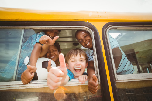 Smiling kids on a school bus with a thumbs up.